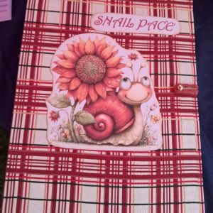 Decorative card showing a sunflower and a smiling snail on a red plaid background, with the text 'SHAIL PACE' at the top.