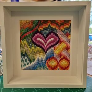 733233155_26930175710012076_9069656610192645552_n | Busy Bees Patchwork Colorful woven textile framed in a white shadow-box display, showcasing rainbow chevron patterns.