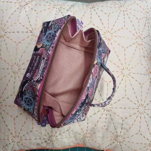 740821610_27050767231286256_7967263596719233760_n | Busy Bees Patchwork Open, patterned zipper pouch with pink lining, laid on a stitched quilt background.