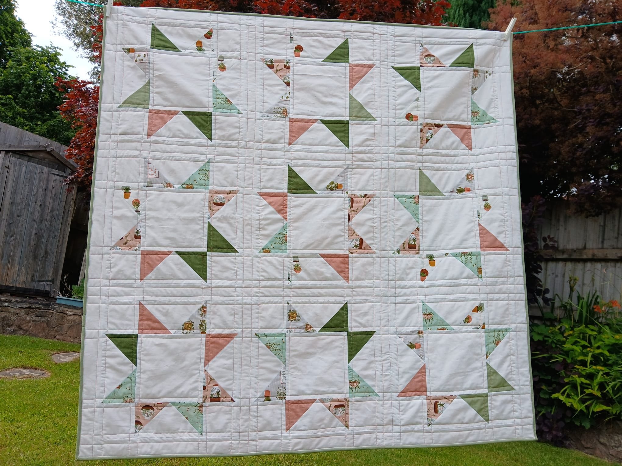 IMG-20260530-WA0003 | Busy Bees Patchwork A quilt with large color-block triangles hangs on a clothesline in a sunny backyard.