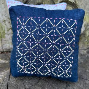 Dark blue denim pouch with pink and white diamond embroidery laid on a weathered wooden surface.",