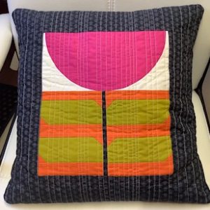 Decorative quilted throw pillow with a pink semicircle on top, green and orange blocks, and a dark blue patterned border.