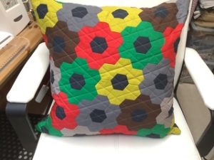 Colorful throw pillow with a geometric flower pattern on a white chair.