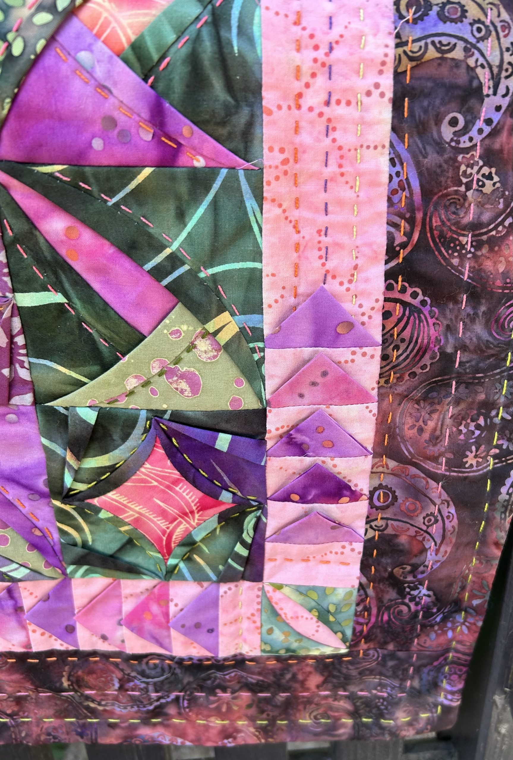 IMG_1720 | Busy Bees Patchwork Close-up of a colorful quilt with pink, purple, and green patches, diagonal stitches, and decorative embroidery.