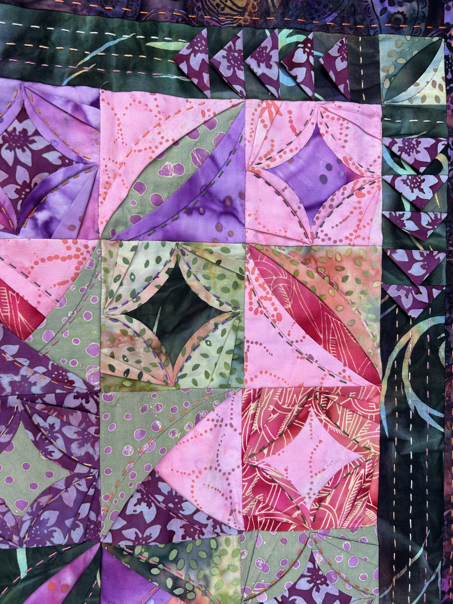 IMG_1721 | Busy Bees Patchwork Patchwork quilt block with purple, pink, and green fabrics arranged in triangular and curved shapes with decorative stitching in orange and other colors.