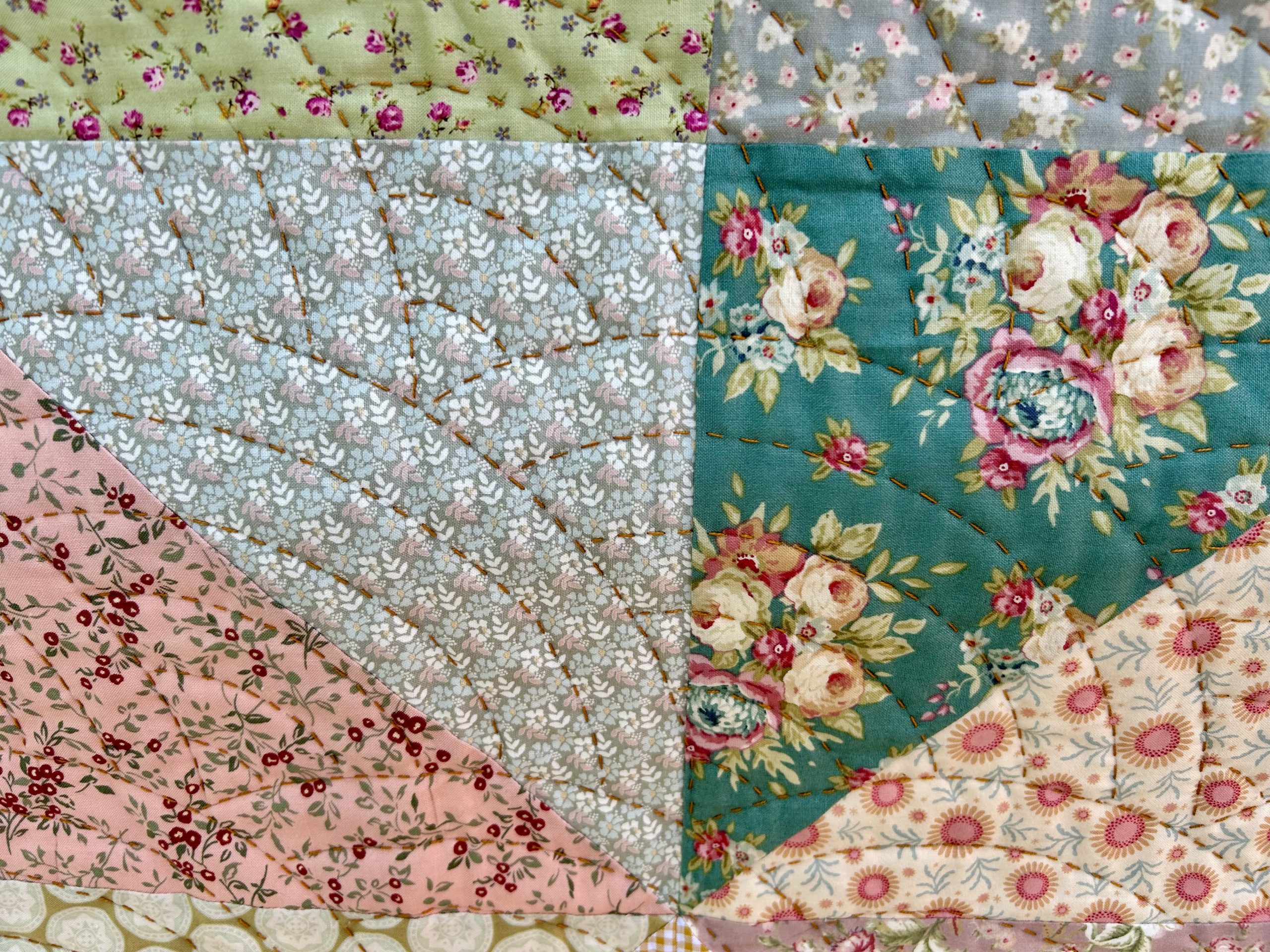 IMG_1722 | Busy Bees Patchwork Close-up of a pastel floral patchwork quilt with visible brown stitching in dashed lines between fabric squares.
