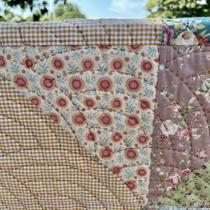 Close-up of a patchwork quilt with yellow gingham and floral fabrics, stitching visible, outdoors.