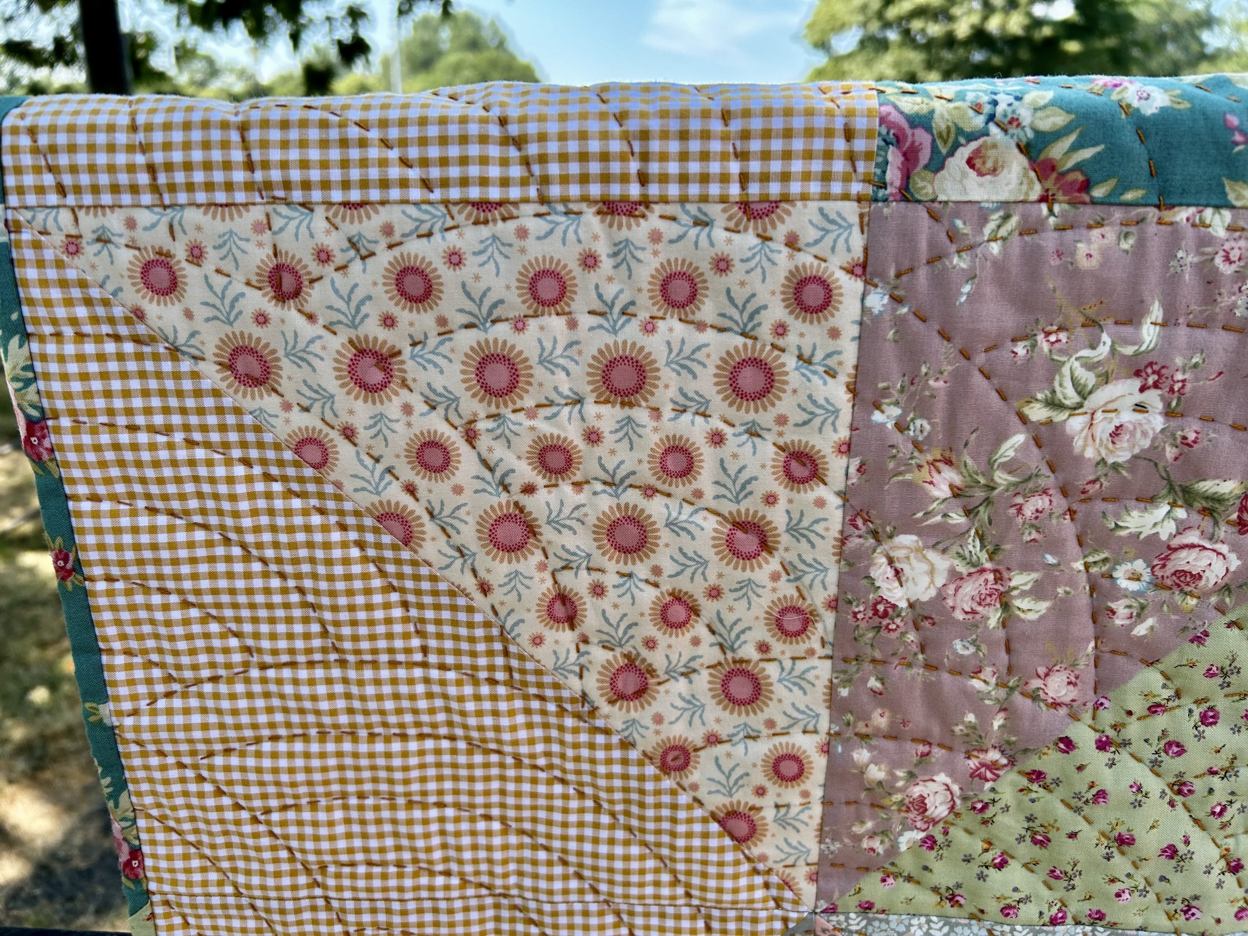 IMG_1725 | Busy Bees Patchwork Close-up of a patchwork quilt with yellow gingham and floral fabrics, stitching visible, outdoors.