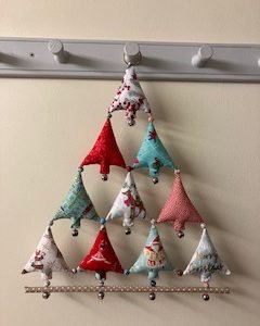 IMG_2808 1 | Busy Bees Patchwork Decorative fabric triangle garland hung from a wall hook rack; red, teal, and cream triangles with small dangling charms.