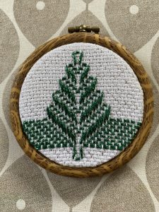 Wooden embroidery hoop holding white fabric with a green leafy stitching design in progress.