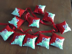 Row of handmade red and mint fabric ornaments with red ribbon ties on a wooden table surface.