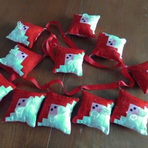 Row of handmade red and mint fabric ornaments with red ribbon ties on a wooden table surface.