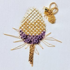 Gold beaded dragonfly pendant with lattice wings and purple body on white fabric.